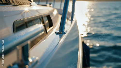 Gleaming yacht side with chrome railings at golden hour, reflecting the serene sparkle of the calm ocean water, symbolizing luxury and peaceful escape