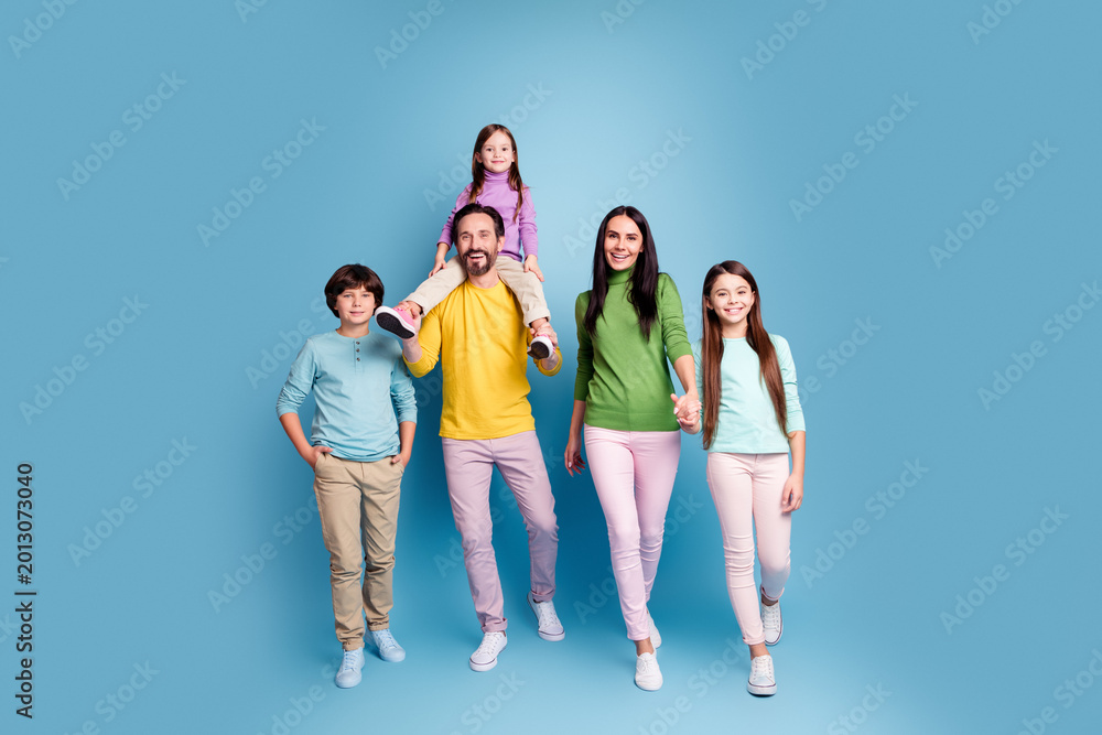 Naklejka premium Happy family portrait of parents and three children walking together in colorful casual clothes against a blue studio background