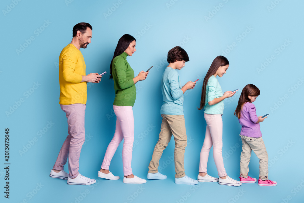 Fototapeta premium Family walking in a row looking at smartphones — parents and children using mobile phones against a blue background