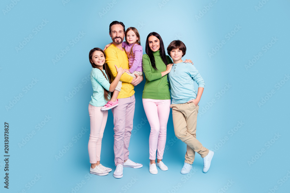 Fototapeta premium Smiling family portrait of parents with three children standing together against a blue background, casual clothing, warm togetherness and happy family moment