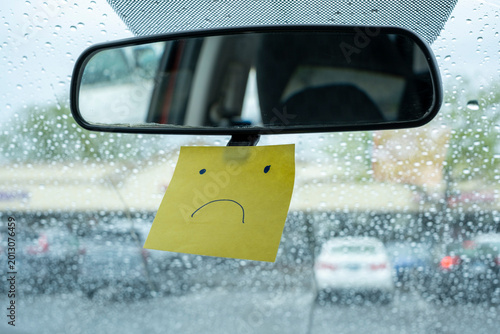 Sad Face Sticky Note on Car Mirror in Rain