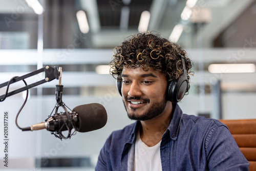 Close-up photo of a young Indian man wearing headphones in an office and talking into a microphone