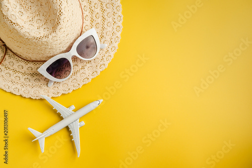 Travel-themed flat lay, summer holiday background. Toy model airplane, sunglasses, sun hat over yellow backgrounds, copy space