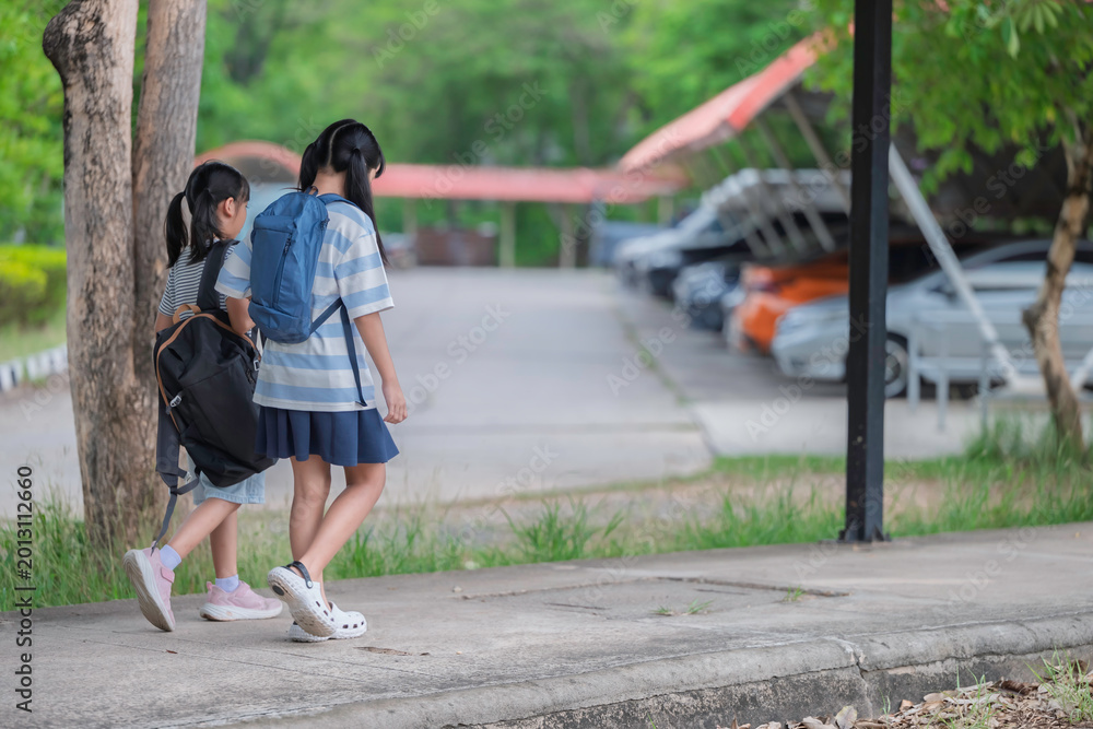 Obraz premium Happy Asian student girls with backpacks walking and running together at school. Back to school concept with kids smiling and having fun outdoors while going to classroom for education and learning.