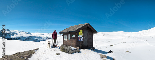 Tableau sur toile Person und Hund an Hütte in winterlicher Hochlandschaft