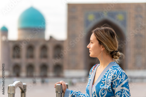 tourist girl in traditional Central Asian clothes against the background of ancient mosques and madrasas in Samarkand, Uzbekistan.