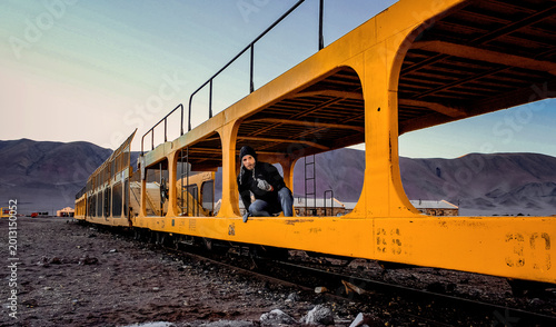 Explorer looking out from inside a massive vibrant yellow industrial train wagon in the remote Martian-like Andean landscape of Tolar Grande, Salta, Argentina, at dawn.