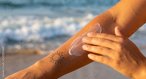 Woman applying sunscreen on arm with sun tattoo at beach