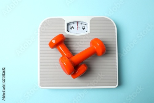 Weight loss concept. Top view photo of scales and dumbbells  on isolated pastel blue background