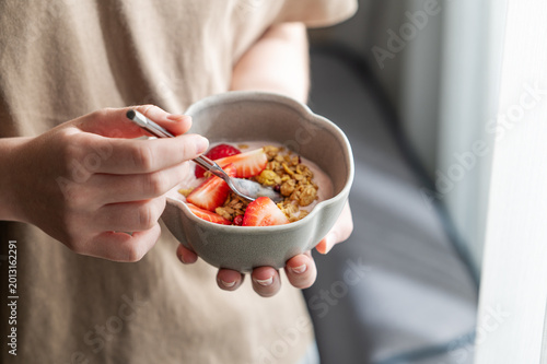 Close-up of a person holding a ceramic bowl with yogurt, fresh strawberries, and granola.