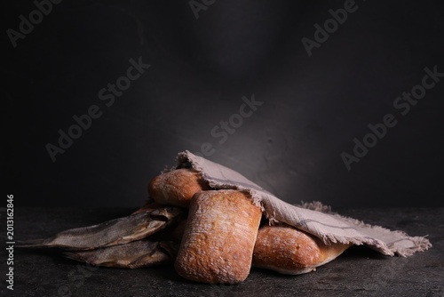 Billede på lærred Dried fish and loaves of bread on black table, closeup