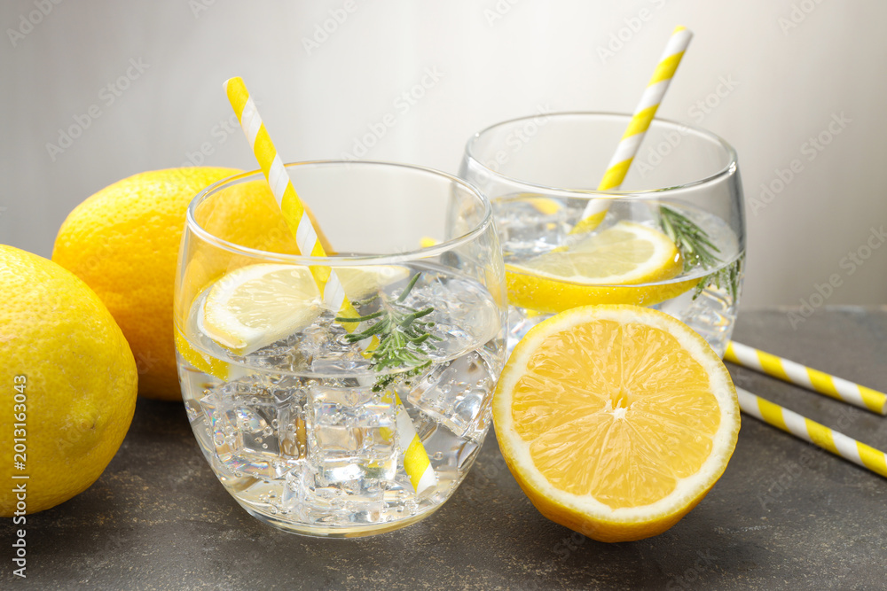 Fototapeta premium Refreshing water in glasses with lemons and rosemary on grey textured table, closeup