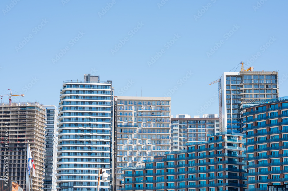 Fototapeta premium High-rise building under construction with tower crane against a clear blue sky.