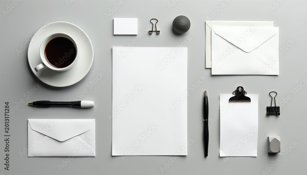 Naklejka premium Flat lay of clean stationery items on gray desk. Blank paper, envelope, pen, coffee cup, business card and clips arranged for mockup or branding presentation.