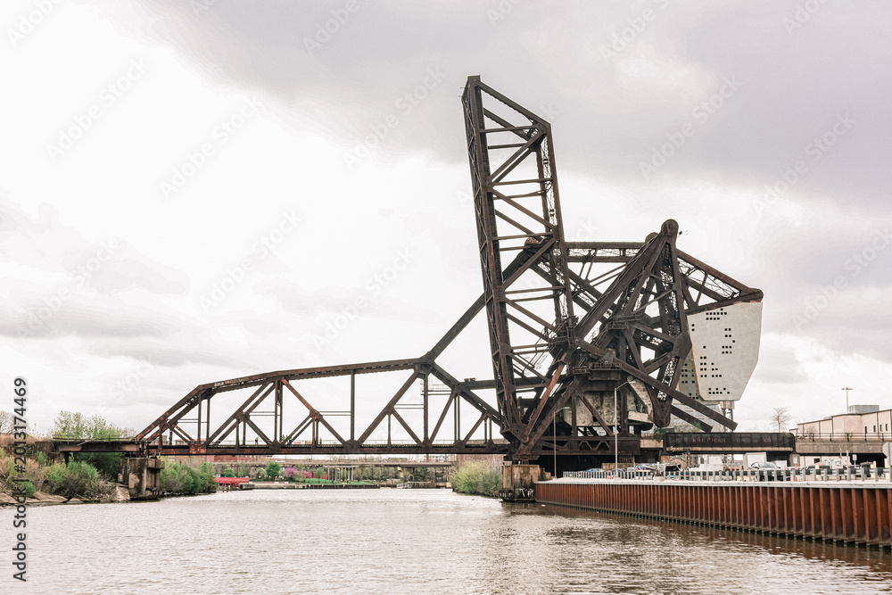 Obraz premium Industrial steel lift bridge over river under dramatic cloudy sky.