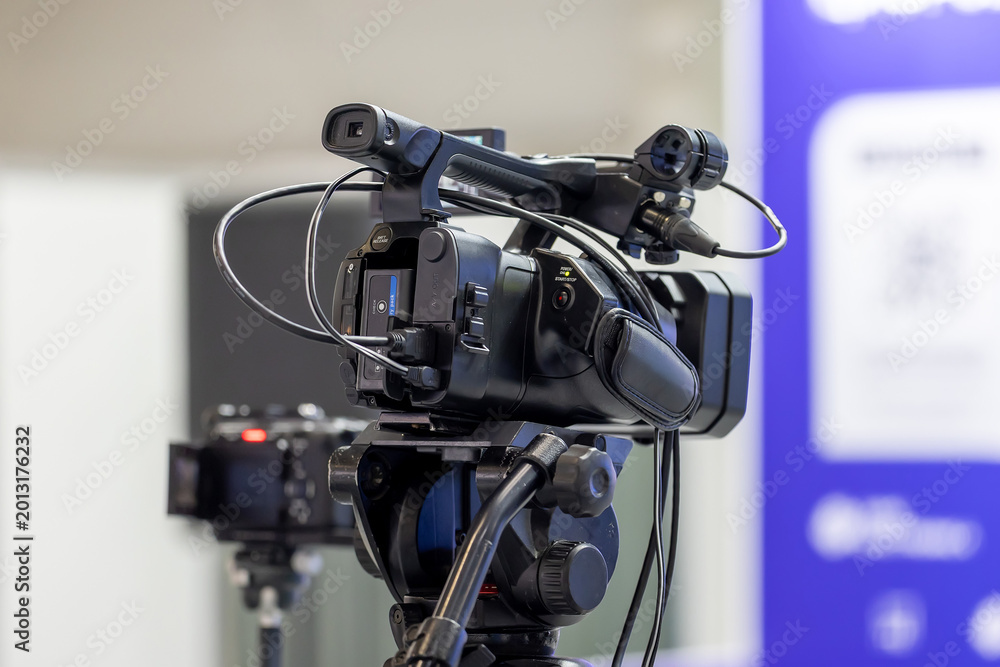 Fototapeta premium Professional video camera on a tripod recording a business conference event in a modern hall. High quality broadcasting equipment for live streaming and media coverage