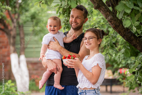 Foto A father and two children hold strawberries in a summer garden at the dacha