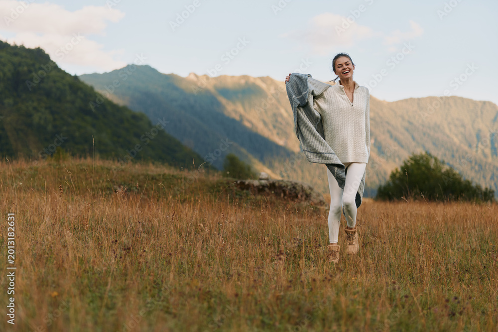 Fototapeta premium Joyful woman outdoors in a sunlit field, wearing casual white outfit, breeze lifting her hair, mountains in the background, relaxed lifestyle moment, natural colors and gentle breeze in air