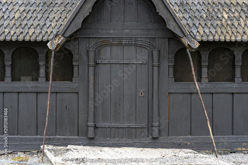 Traditional Norwegian stave church surrounded by spring countryside and forested hills under dramatic cloudy sky in Telemark, Norway. Dark wooden medieval-style architecture. 