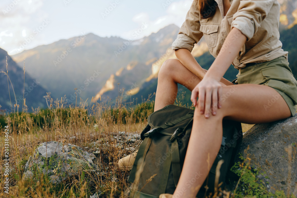 Naklejka premium Cheerful woman outdoors, resting on a rock in a mountain landscape, wearing casual hiking clothes, sunlit moment, relaxed posture, natural tones, expansive scenery. Calm.