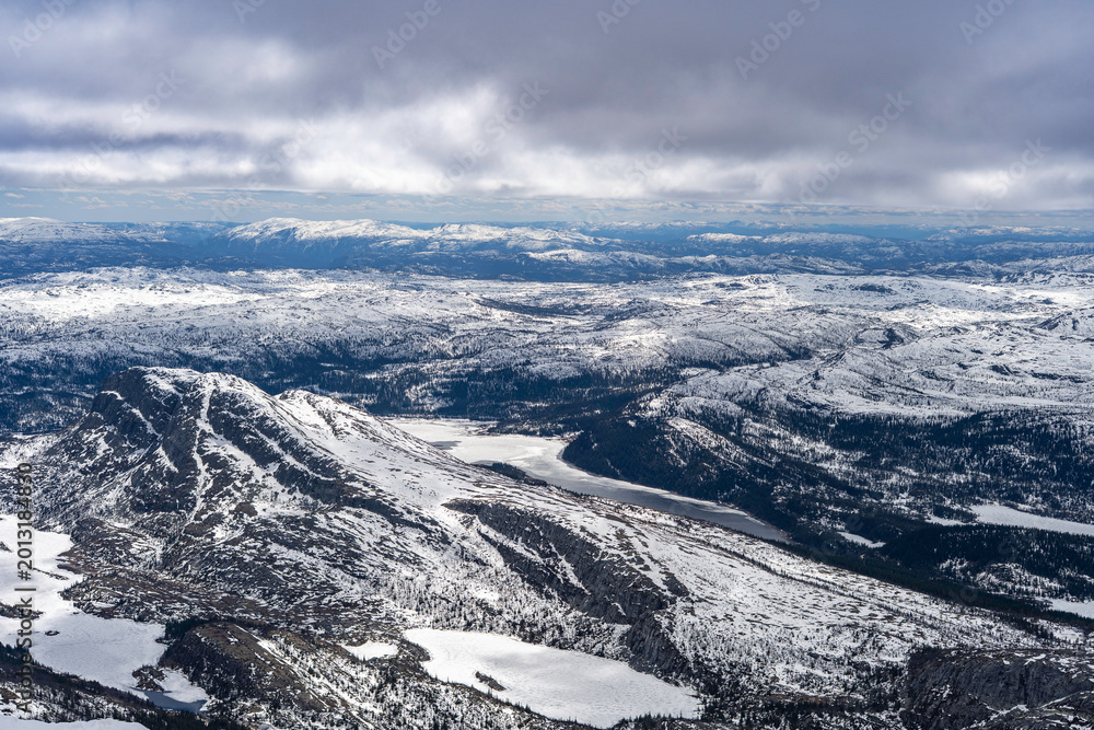 Fototapeta premium Panoramic view from the summit of Gaustatoppen at 1,850 meters above sea level. Snow-covered mountain plateaus, rocky ridges, and vast landscapes of southern Norway under a dramatic cloudy sky.