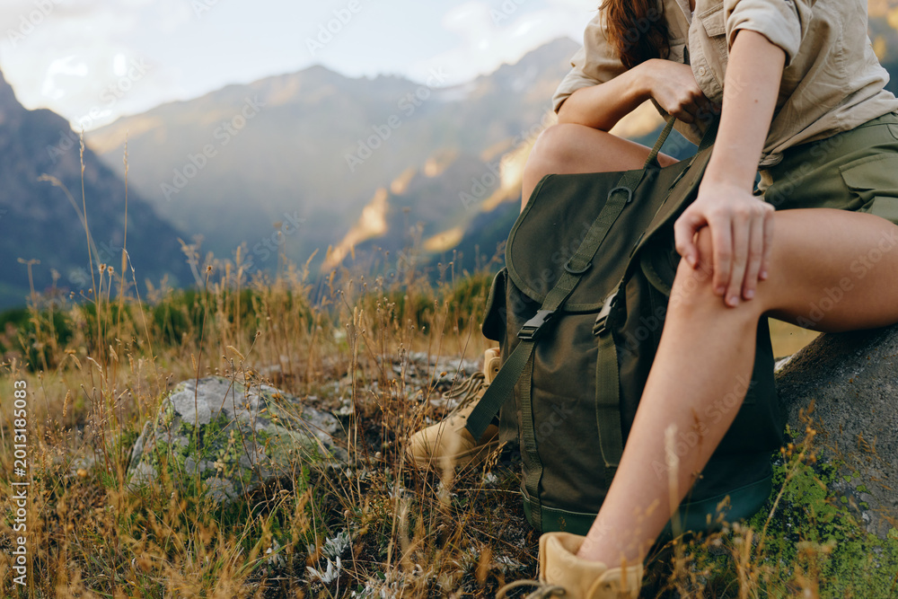 Fototapeta premium A woman sitting during a hiking moment in a sunlit mountain scenery, wearing casual clothing with a backpack nearby. Emphasizes outdoor lifestyle, nature, and calm.