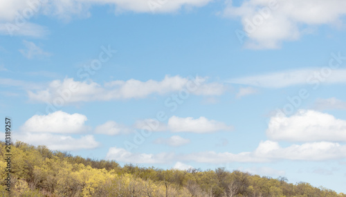Idyllic country spring background with cloudy sky above hilly forest