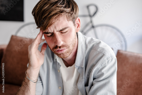 Foto A young man sits on a couch at home holding his temple and wincing from a headache