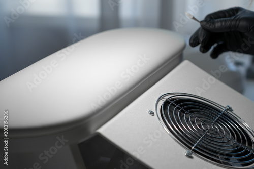 Close-up view of a technician's gloved hand making adjustments to a modern air purifier, showcasing the fan grill and sleek surface design