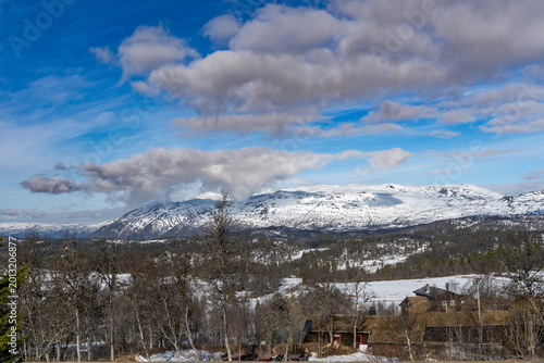Amazing view of Norwegian mountains. Stunning landscape with traditional wooden houses and snowing tops on the horizon.