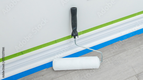 Fotografia Paint roller with a white cover resting on a floor near freshly applied painter'