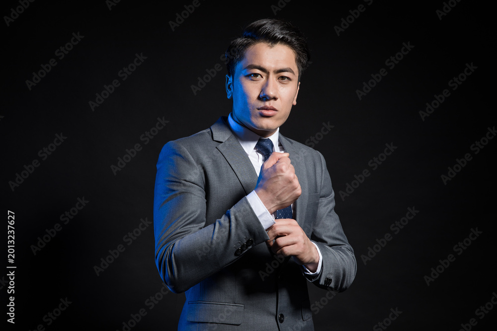 Naklejka premium Confident young businessman adjusting tie on dark background