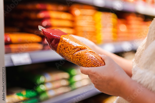 Obraz na plátně Woman choosing packaged red lentils in supermarket aisle, customer holding dry l