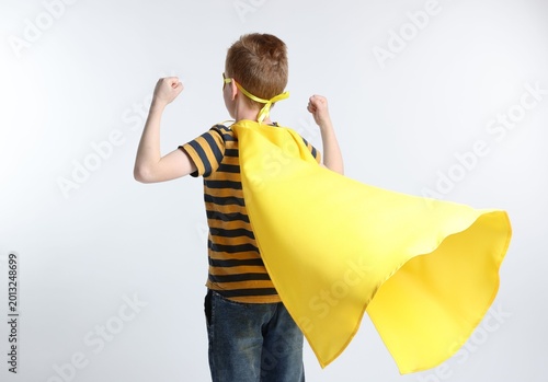 Fotografía Little boy in superhero costume showing muscles on white background, back view