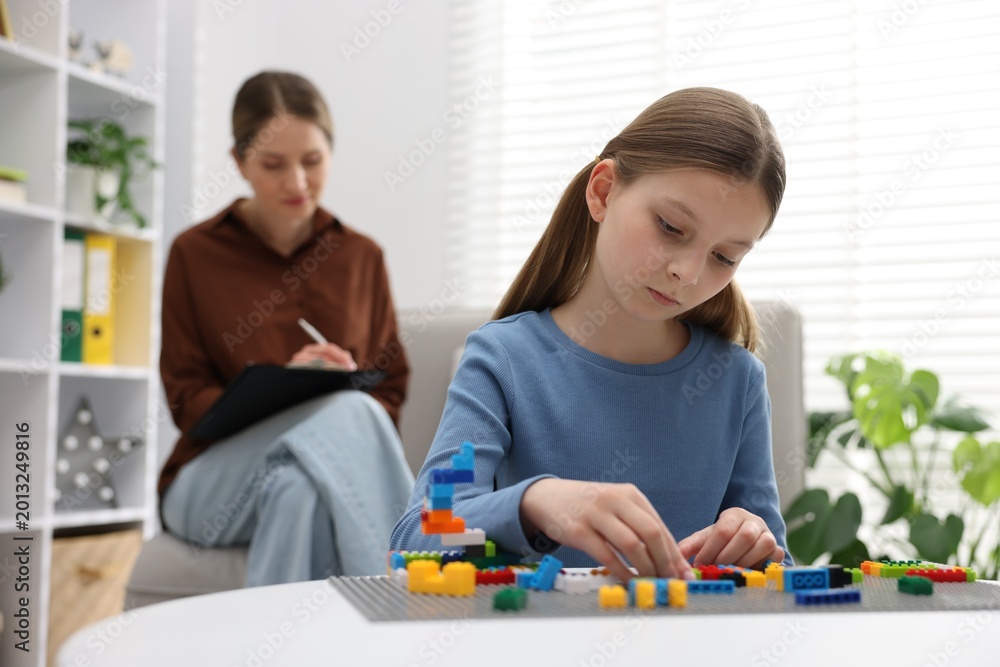 Fototapeta premium Girl playing with toys at white table during consultation with professional child psychologist indoors, selective focus