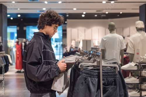 Foto Young teenage boy with curly hair browsing shorts selection at modern menswear clothing store
