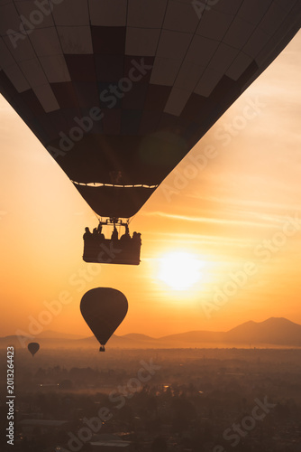 Hot air balloons floating over Teotihuacan Mexico at sunrise with silhouettes against a vibrant orange sky