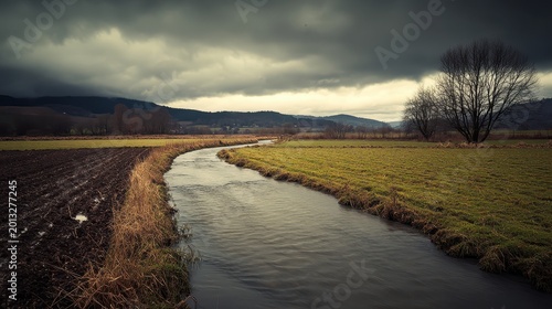 A winding river through agricultural fields under a dramatic overcast sky, showcasing natural textures and rural landscape