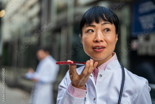 Foto Female doctor dictating voice message on smart phone outdoors