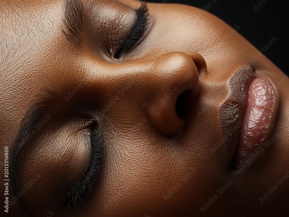 Naklejka premium Ultra-detailed macro of a woman's face with radiant dark skin, glossy lips and long lashes — luxury beauty and skincare editorial concept for cosmetic brands in 2026.