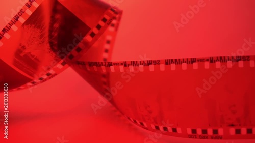 35mm negative photographic film in rotation in red room, camera darkroom. Slightly rolled film strip isolated on red background. Analog film strips. Analog photography. Close-up. 