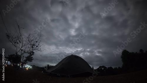 Dramatic time lapse of dark storm clouds moving rapidly over a silhouetted camping tent at night.