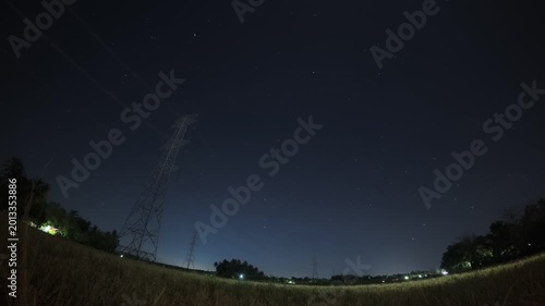 Cinematic time lapse of a starry night sky with stars moving over silhouetted electric pylons and power lines.