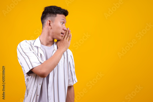 Fotografie Young Asian Man Whispering Secret with Hand Near Mouth, Looking Aside with Curio