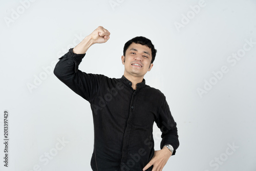 Confident Asian man raising one fist in victory pose on white background