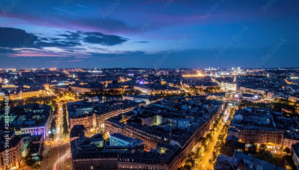 Obraz premium Aerial cityscape at dusk with illuminated buildings and roads, under a dramatic, colorful sky