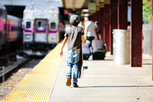 Foto Rear view of a young boy carrying a skateboard on a train station platform in Boston during a family road trip across America