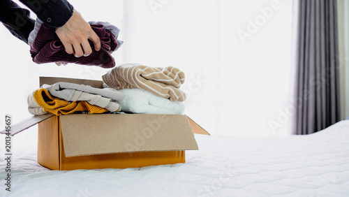 Person packing folding clothes into cardboard box for donation at home. Charity, decluttering, recycling and sustainable lifestyle concept.
