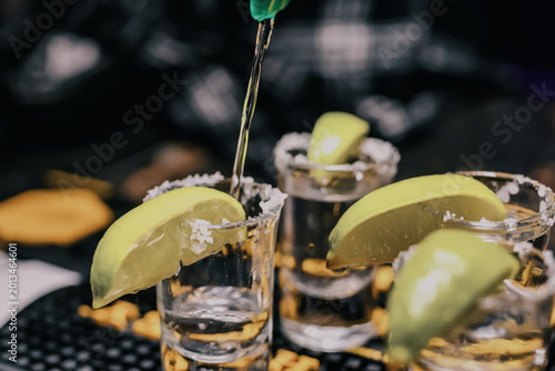 Premium tequila pours into salt-rimmed shot glasses with fresh lime wedges at upscale nightclub bar, capturing vibrant party energy for alcohol branding, nightlife marketing, and hospitality ads