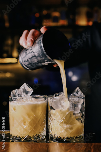 Luxury cocktails with ice are poured into crystal glasses at elegant nightclub bar, showcasing premium mixology experience and upscale nightlife concept for beverage branding and hospitality ads